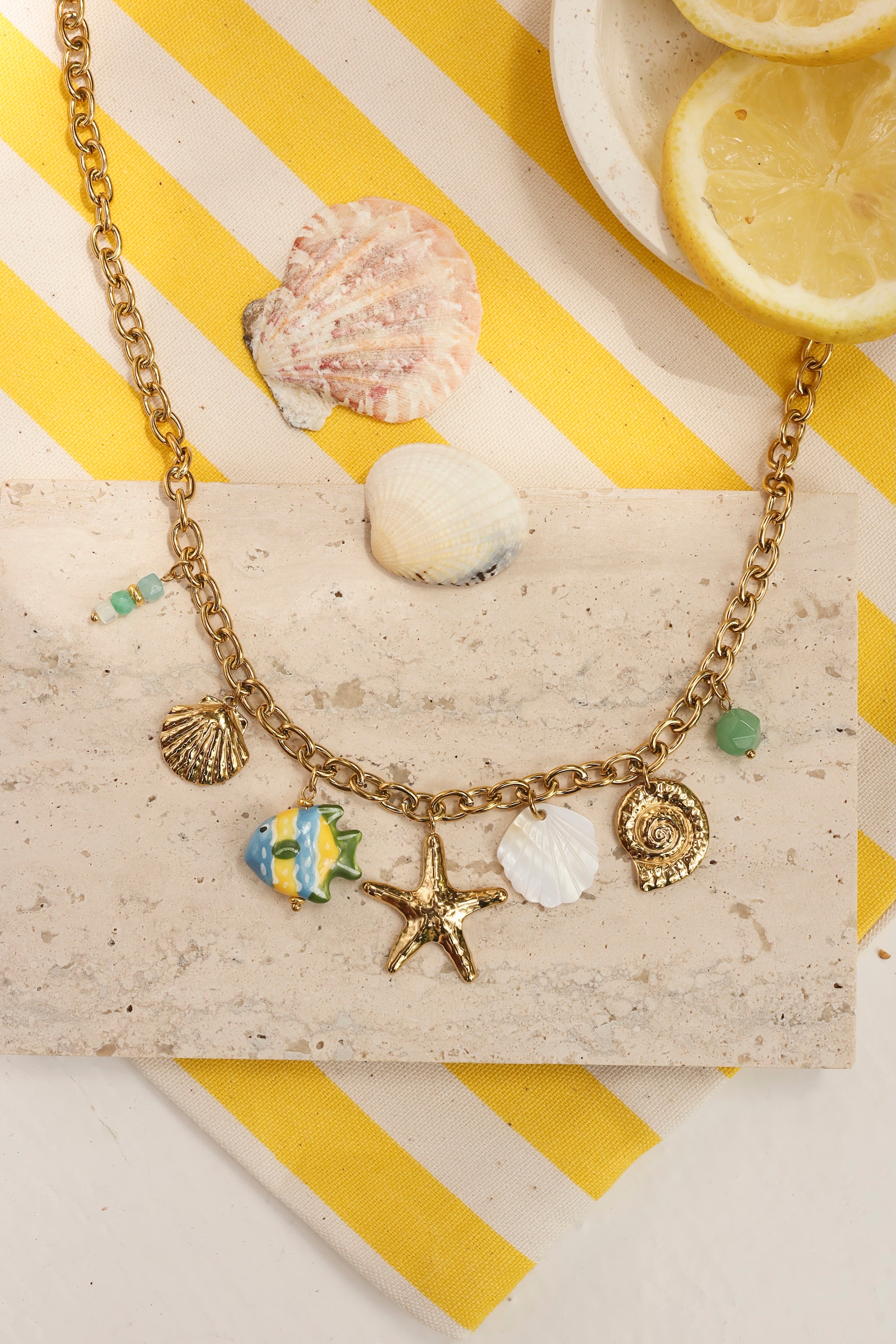 Collier doré Livio chaîne en maille avec pendentifs coquillages, étoile de mer, coquillage en nacre, poisson et pierres naturelles - Bijou photographié dans un décor estival