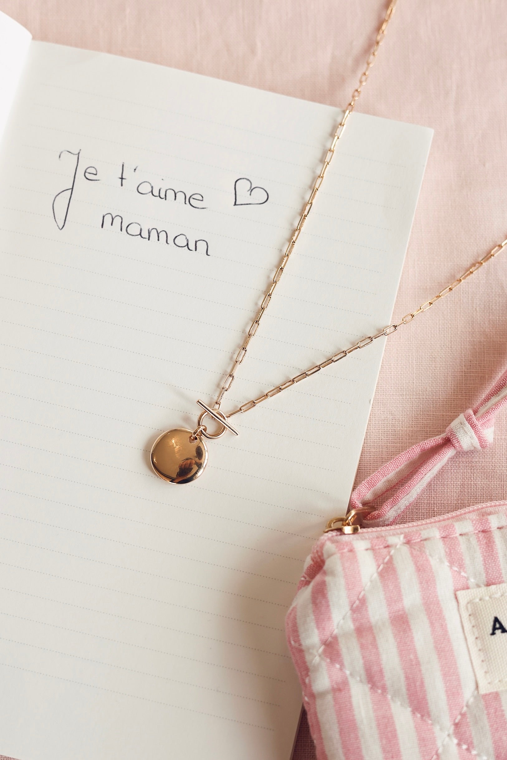 Collier en maille fine à détail T-bar orné d’une médaille ronde bombée pour gravure Natacha - Bijou photographié sur un livre où il y a écrit "je t'aime maman"