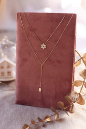 Collier doré Neije pendentif flocon de neige serti de zircons - Bijou photographié sur un présentoir en lin rose foncé