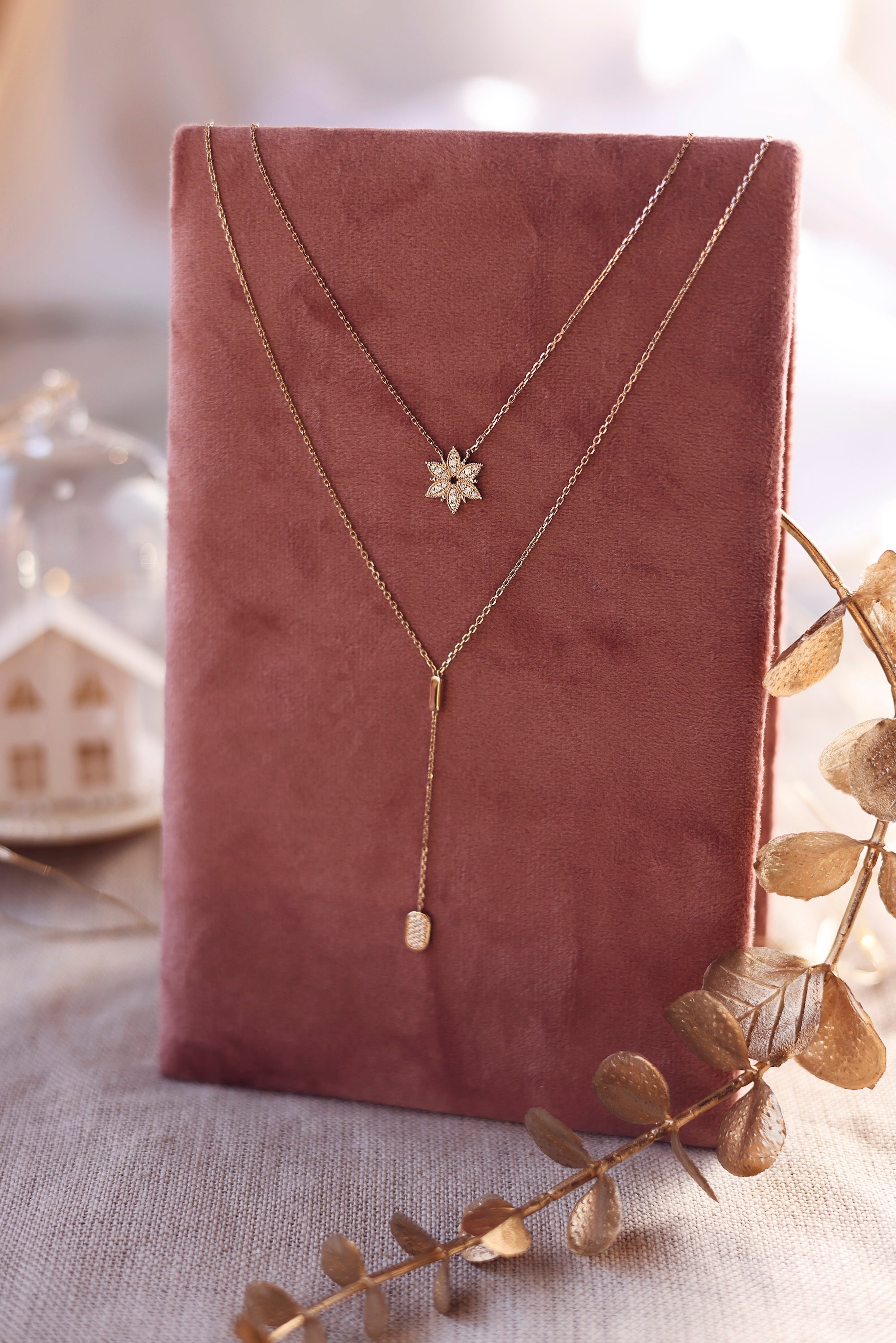 Collier doré Neije pendentif flocon de neige serti de zircons - Bijou photographié sur un présentoir en lin rose foncé