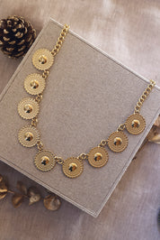 Collier statement doré Sidonie - Bijou photographié sur un présentoir en lin gris posé sur un tissu beige avec des décorations de Noël