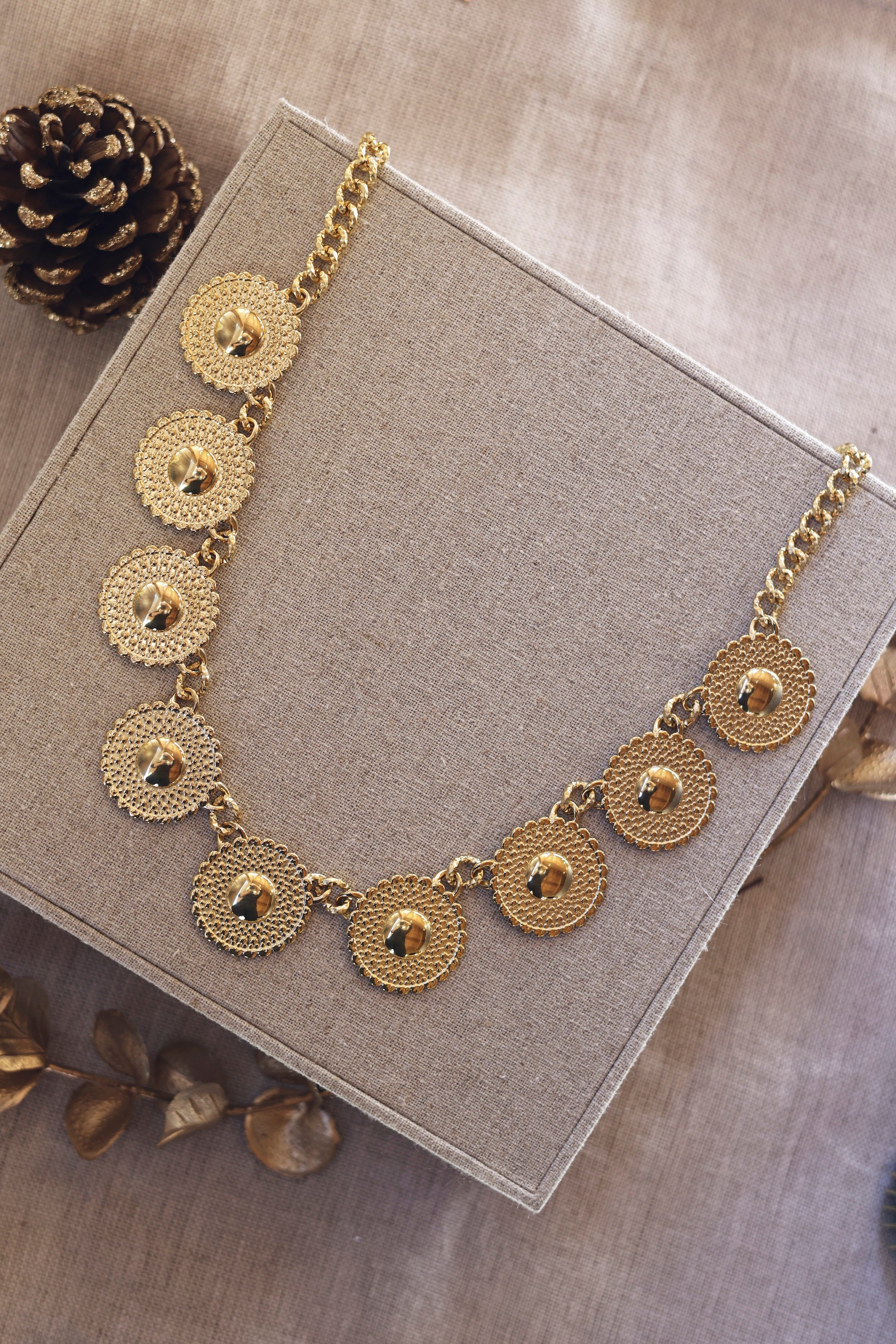 Collier statement doré Sidonie - Bijou photographié sur un présentoir en lin gris posé sur un tissu beige avec des décorations de Noël