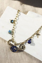 Collier en maille doré Alyssa avec pendentifs lunes, soleil, planètes et étoiles - Bijou photographié sur un présentoir en marbre blanc posé sur un tissu en lin beige