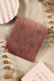 Collier doré Colline trèfles - Bijou photographié sur un présentoir en velours rose foncé posé sur un tissu en lin avec des feuilles décoratives dorées