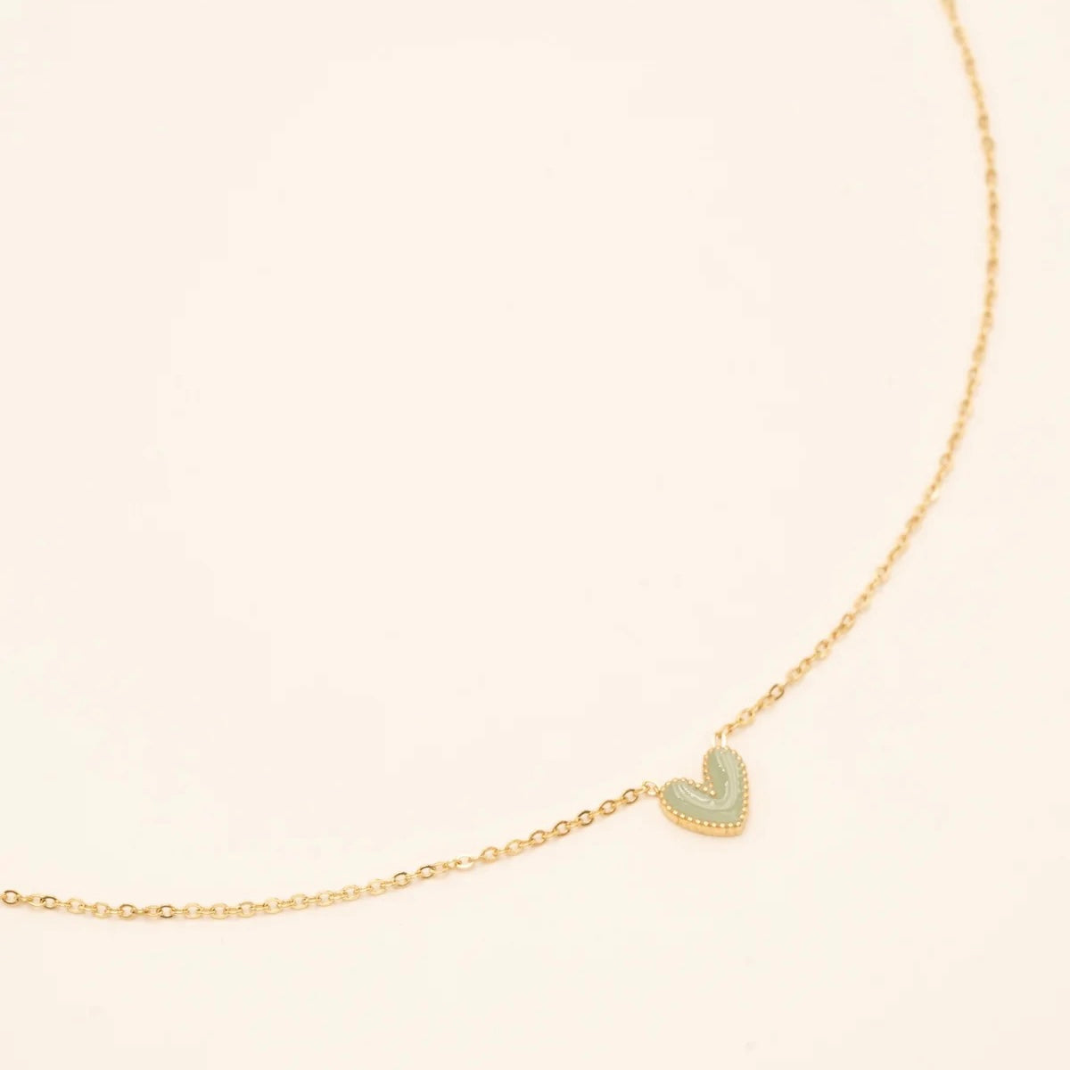 Collier Petit Coeur pour enfant doré pendentif coeur vert - Bijou photographié sur fond beige