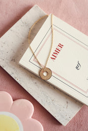 Collier personnalisable doré Isao chaîne fine et médaille cible à graver - Bijou posé sur un livre