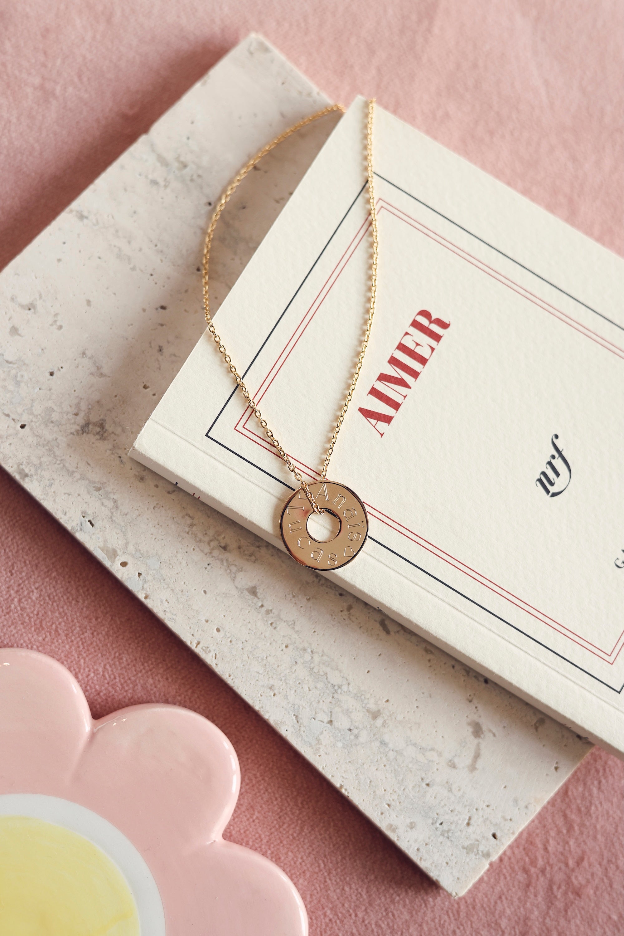 Collier personnalisable doré Isao chaîne fine et médaille cible à graver - Bijou posé sur un livre