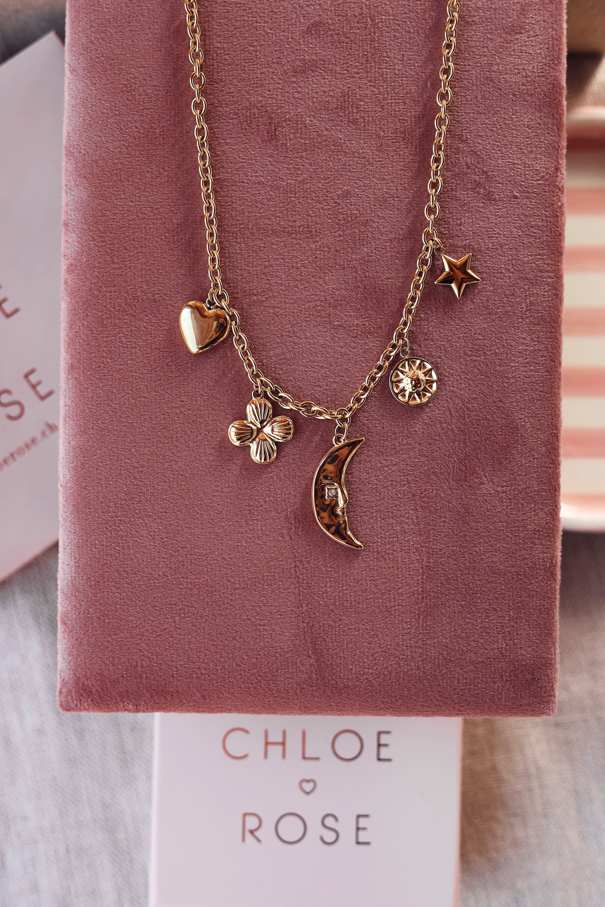 Collier doré Lorna en maille avec pendentifs lune, fleur, soleil, coeur et étoile - Bijou photographié sur un présentoir en velours rose foncé