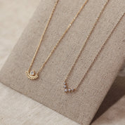 Collier doré Madysson en plaqué or avec pendentif contemporain, collection Chloé Rose Genève - Bijou photographié sur présentoir en lin gris