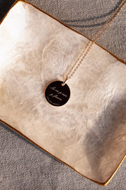 Collier doré Mantra lotus gravé "Là où je suis, je fleuris" - Bijou photographié dans une coupole en nacre blanche côté gravure