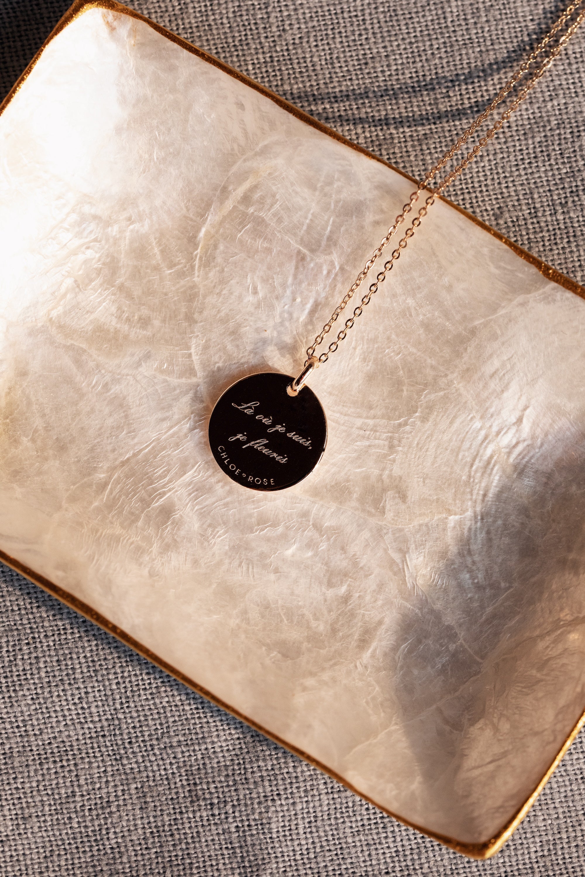 Collier doré Mantra lotus gravé "Là où je suis, je fleuris" - Bijou photographié dans une coupole en nacre blanche côté gravure