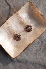 Collier doré Mantra lotus gravé "Là où je suis, je fleuris" - Bijou photographié dans une coupole en nacre blanche côté symbole