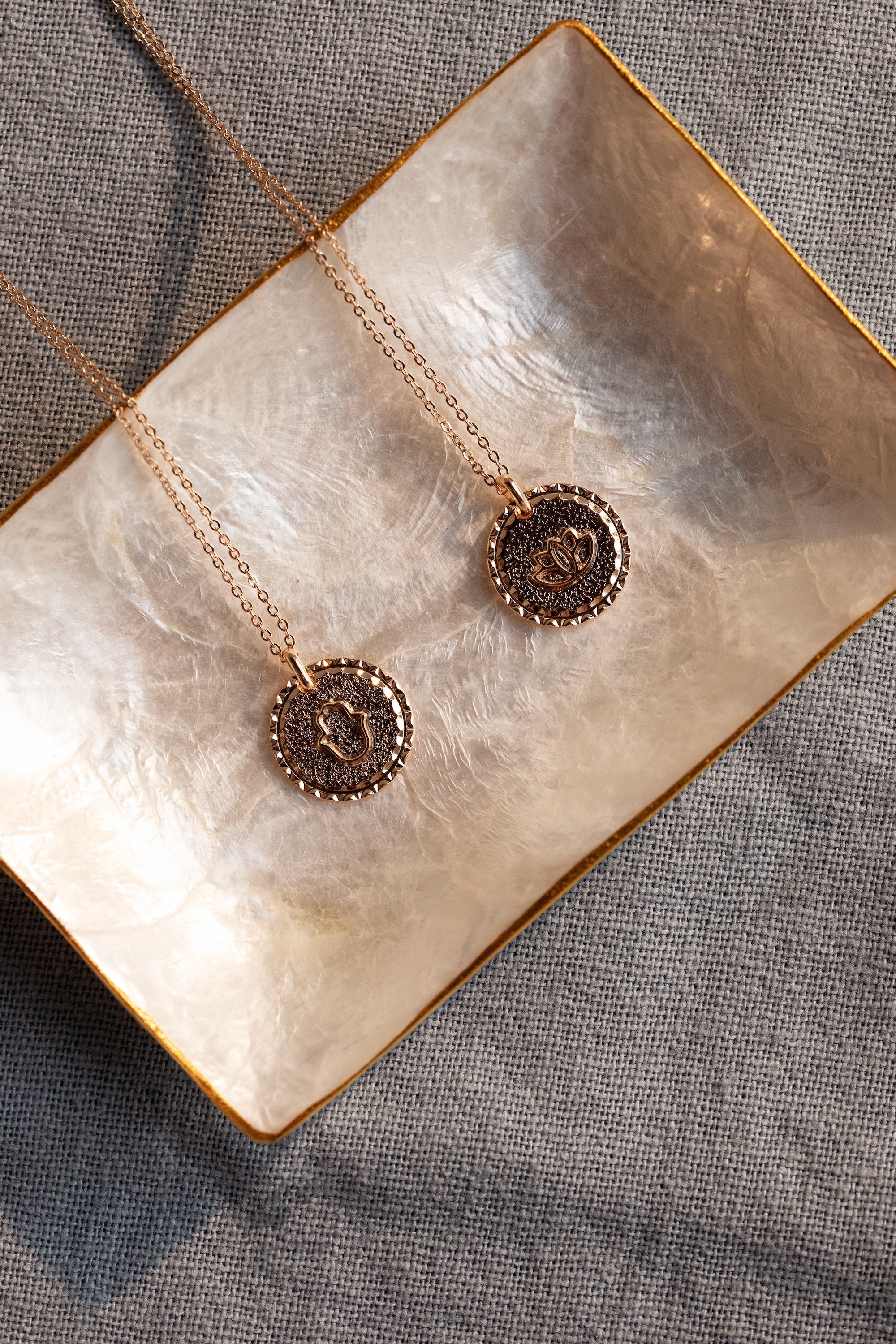 Collier doré Mantra lotus gravé "Là où je suis, je fleuris" - Bijou photographié dans une coupole en nacre blanche côté symbole