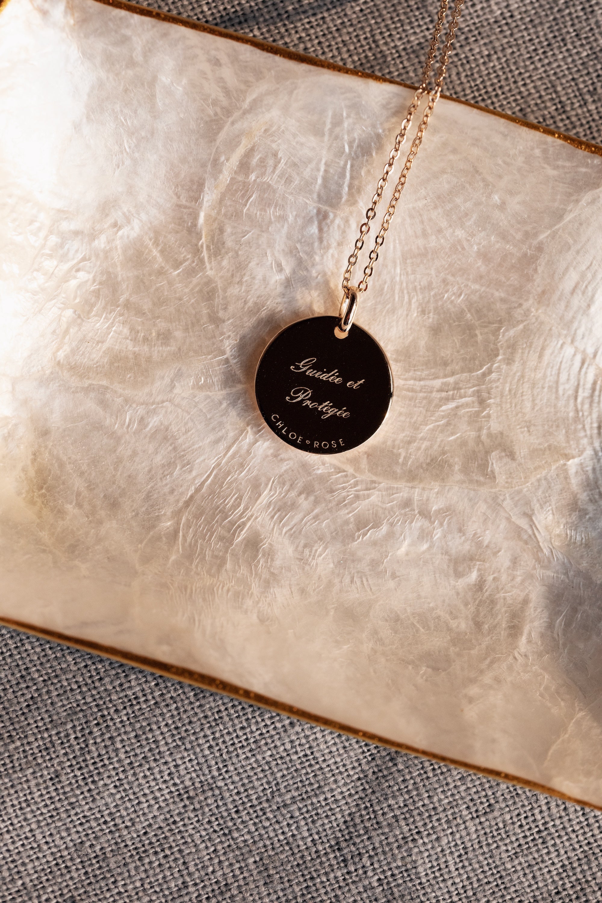 Collier doré Mantra main de Fatma gravé "Guidée et protégée" - Bijou photographié dans une coupole en nacre côté gravure
