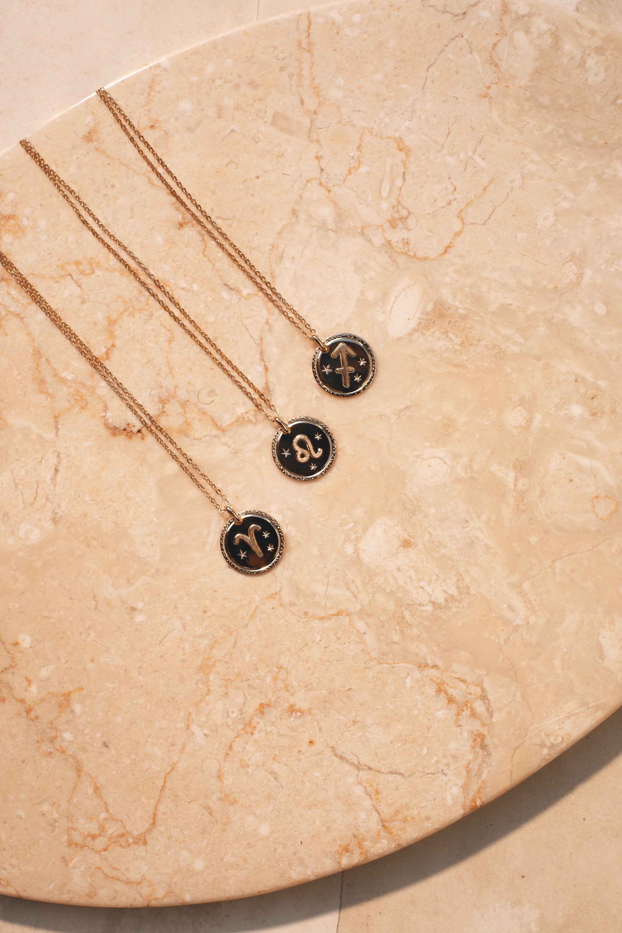  Collier doré signe du zodiaque Bélier - Bijou photographié sur une coupole en pierre beige marbrée