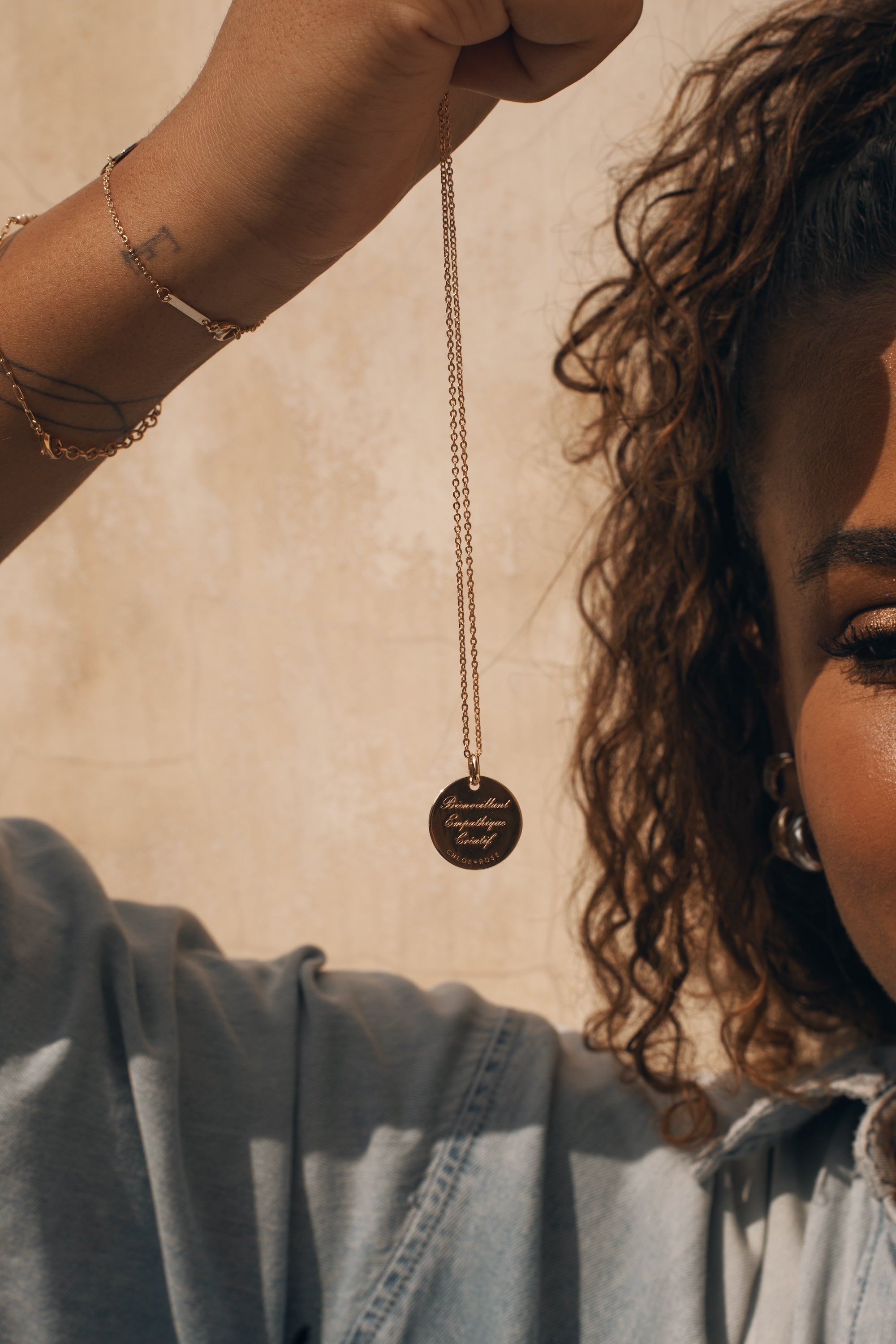 Collier doré signe du zodiaque Poissons - Bijou suspendu dans la main d'une mannequin aux cheveux bouclés