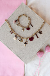 Collier doré Swanne maille avec pendentifs trèfle, rose, bouche, étoile, coeur et&nbsp;amulette avec inscription "amour" - Bijou photographié sur un présentoir en lin gris