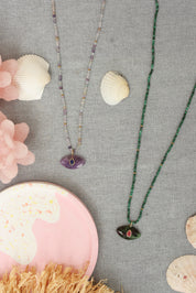 Collier sur fil doré Thelma malachite composé de perles en malachite avec pendentif en forme d'œil en rubis zoïsite orné d'une goutte en rhodonite - Bijou photographié dans un décor estival