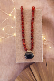 Collier statement doré Isis cornaline en pierres naturelles et zircons - Bijou photographié sur un présentor en lin gris