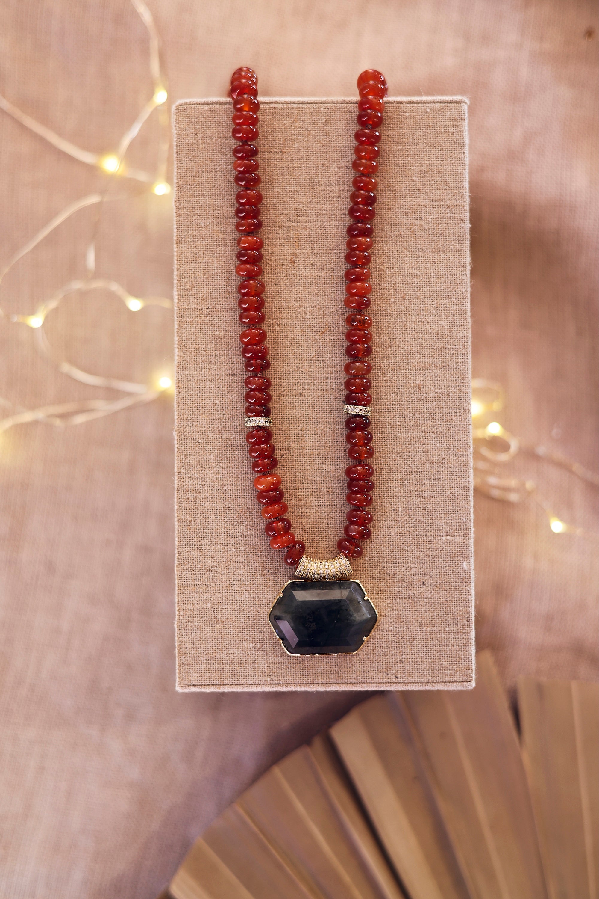 Collier statement doré Isis cornaline en pierres naturelles et zircons - Bijou photographié sur un présentor en lin gris