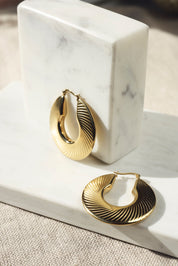 Créoles dorées Helda striées - Bijou photographié sur un présentoir en marbre blanc