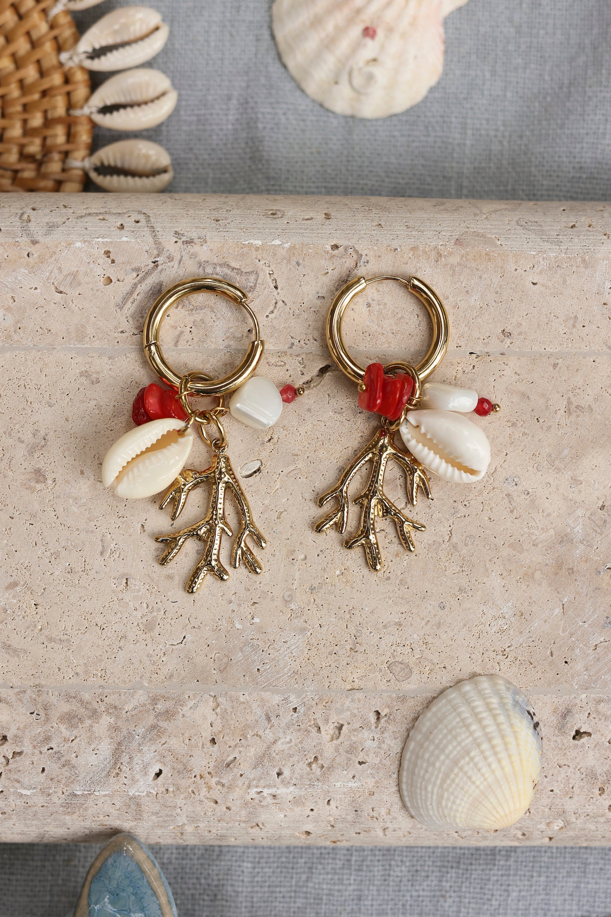 Boucles d'oreilles mini créoles dorées Lowen avec pendentifs corail, coquillage et pierres naturelles - Bijou photographié dans un décor estival