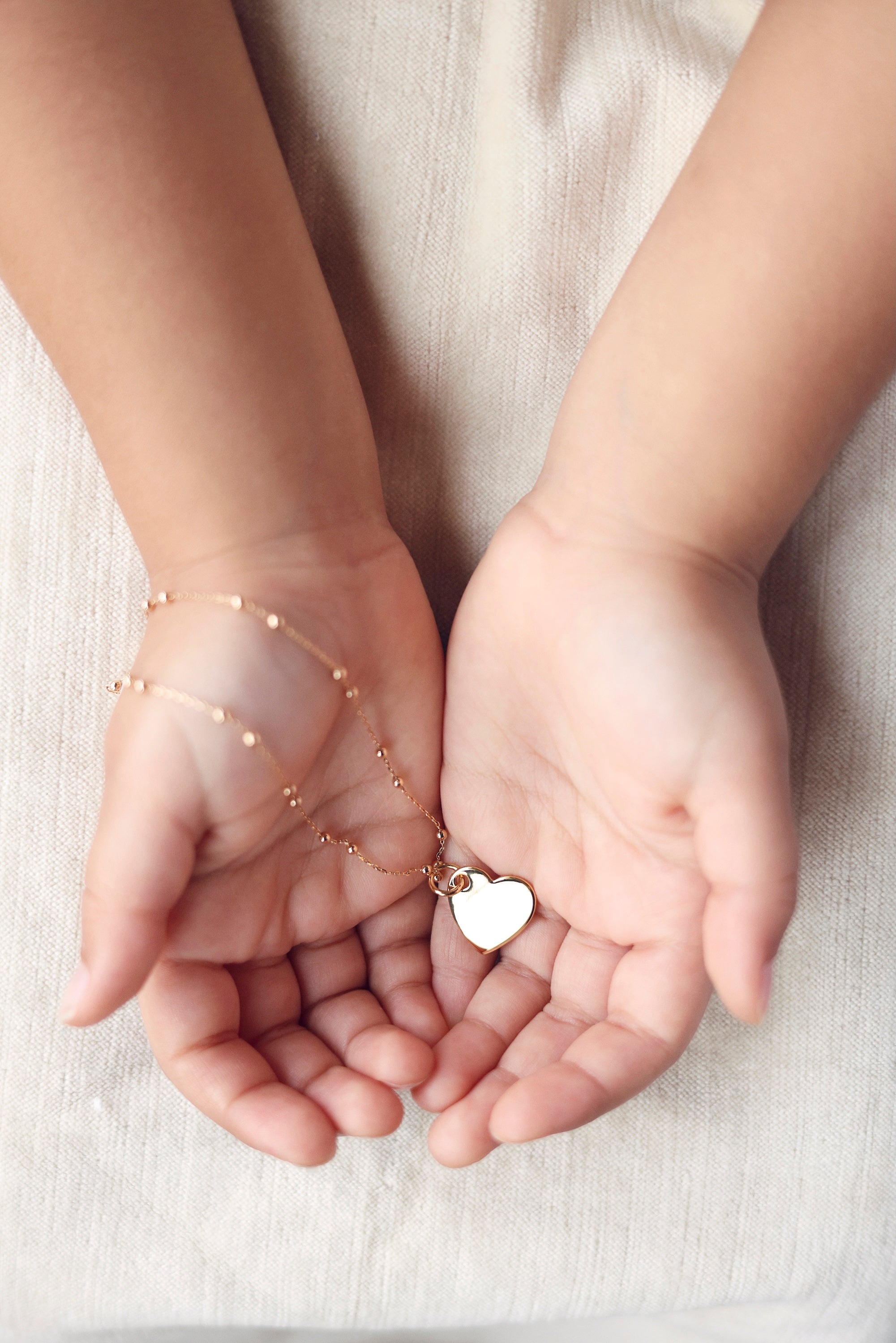 Médaille dorée Amour S en forme de cœur pour gravure - Bijou porté dans les mains d'une enfant