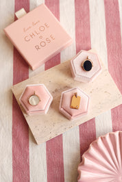 Médaille réversible ronde dorée Joy avec un côté en nacre et un côté à graver - Bijou photographié sur un présentoir rose sur une pierre rectangulaire avec des décorations roses et une boîte chloe rose