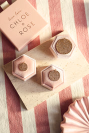 Médaille réversible dorée avec une face texturée et une face lisse pour gravure Nessie M - Bijou photographié dans un décor rose et blanc avec les différentes tailles de médailles Nessie