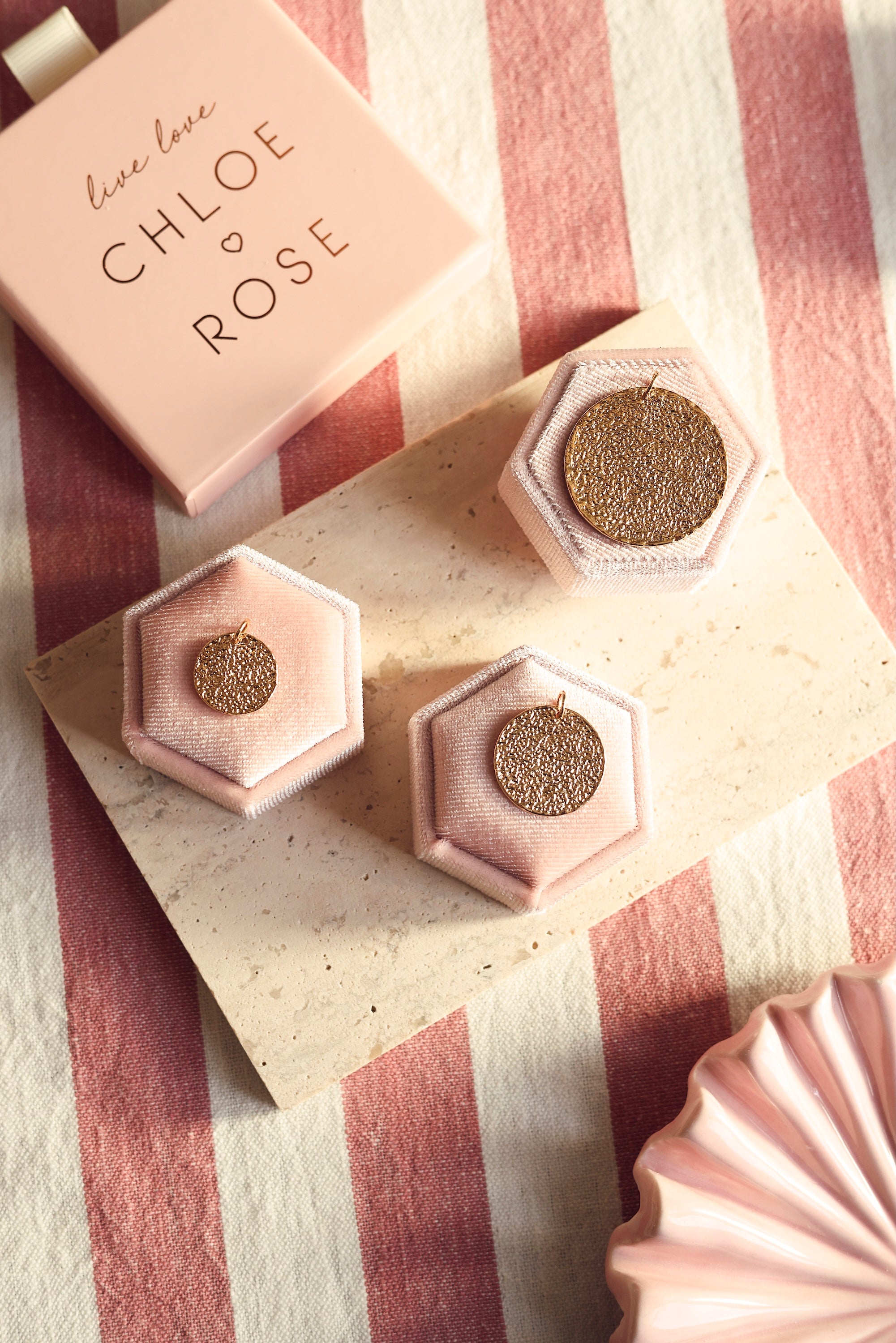 Médaille réversible dorée avec une face texturée et une face lisse pour gravure Nessie M - Bijou photographié dans un décor rose et blanc avec les différentes tailles de médailles Nessie