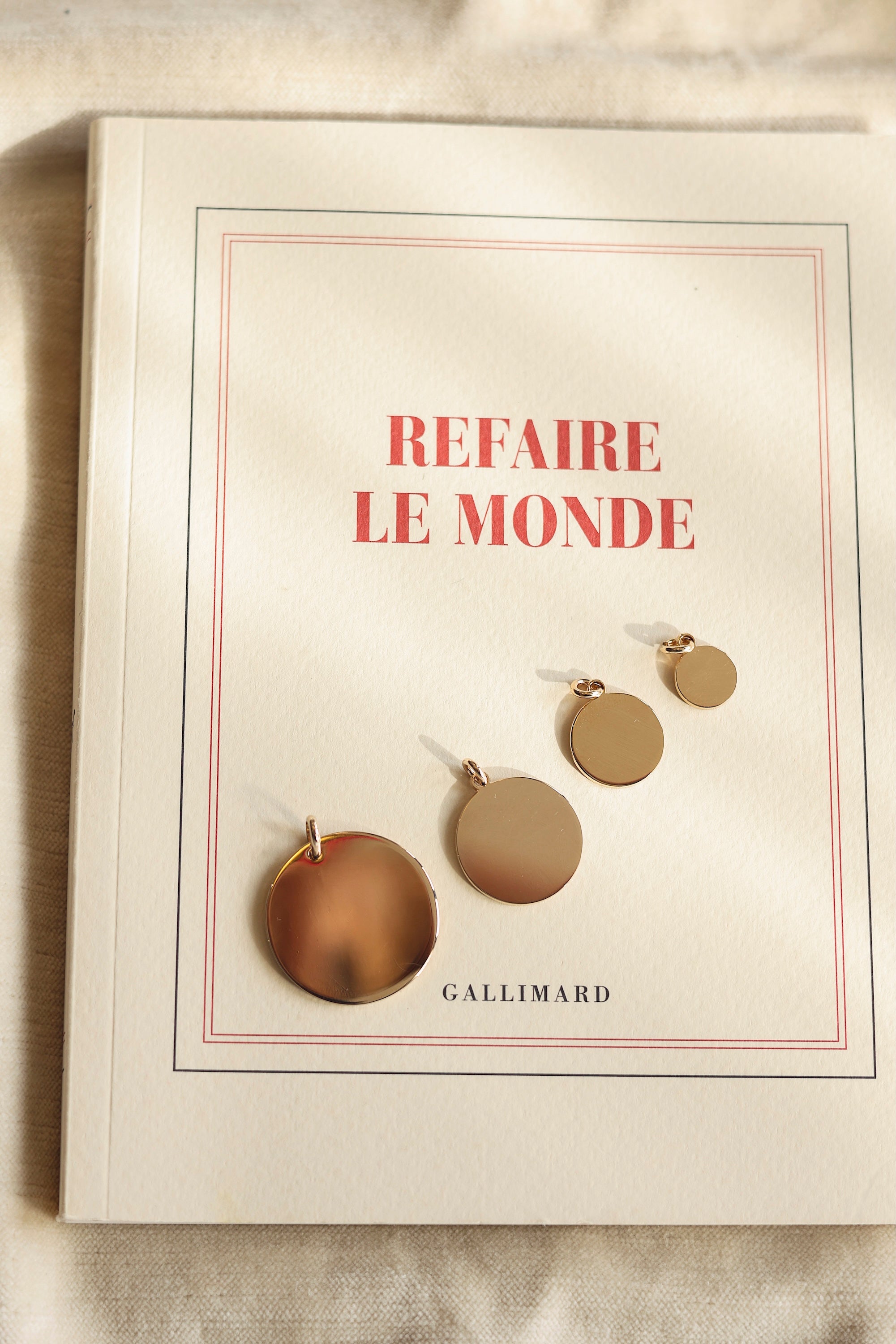 Médaille ronde simple dorée pour gravure Alba M - Bijou photographié sur un livre