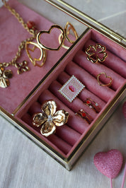 Pin's doré timbre - Accessoire photographié dans une boite à bijoux en velours rose